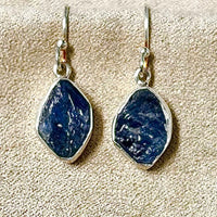 Pair of blue rough sapphire earrings on a beige velveteen background