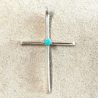 Silver cross pendant with a turquoise stone on a beige background